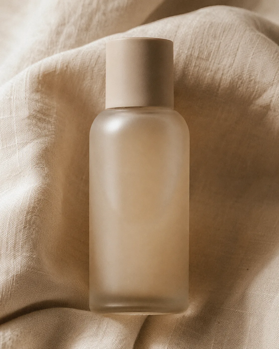 Frosted Méra bottle resting on folded oat-coloured linen